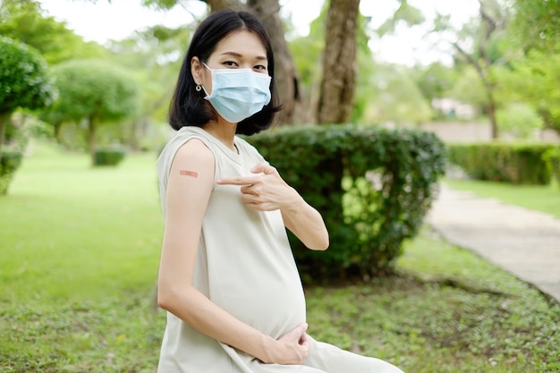 Eine schwangere Mutter in einem Kleid zeigt nach der Impfung ein Pflaster am Oberarm.