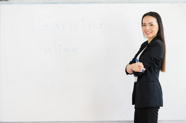 Eine schwarz gekleidete asiatische Lehrerin steht vor einem Whiteboard vor einem Klassenzimmer an der Universität. Bildungskonzept, Abschluss, Hochschullehrerkarriere