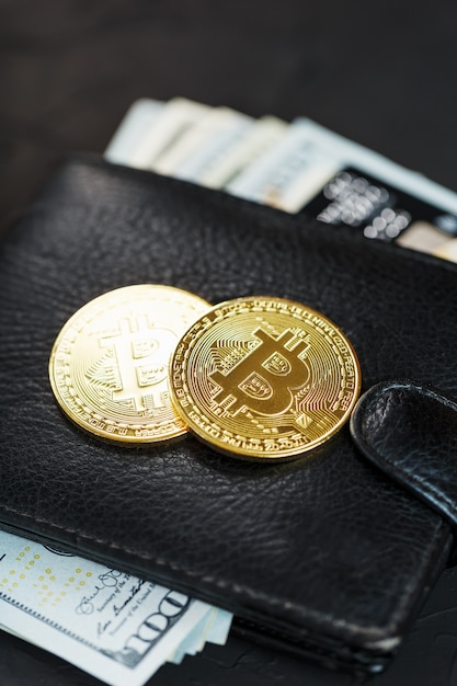 Eine schwarze Brieftasche mit Dollars, E-Cards und Bitcoins auf schwarzer Textur.
