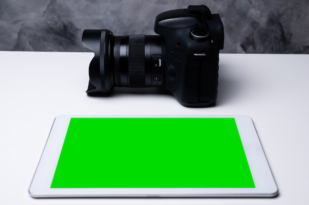 Eine schwarze Digitalkamera und ein Tablett mit leerem Bildschirm auf einem Tisch.