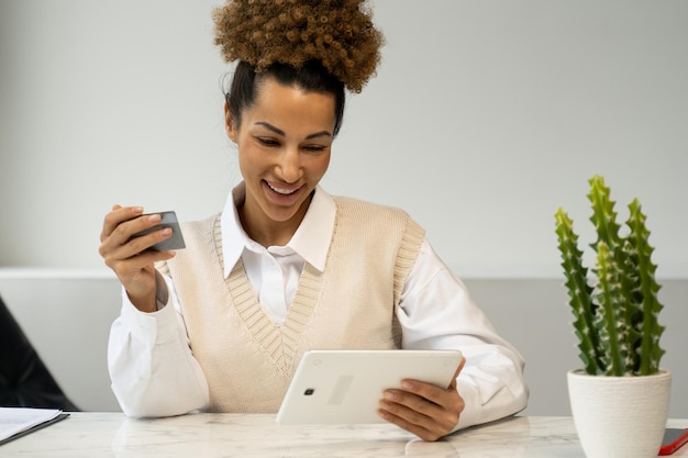Eine schwarze Frau, die eine Kreditkarte hält, nimmt eine Online-Zahlung mit einem Tablet vor
