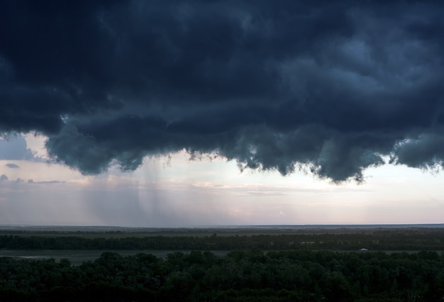 Eine schwarze Gewitterwolke über der Stadt, aus der eine starke Regenwasserwand ergießt. Ein schweres Gewitter