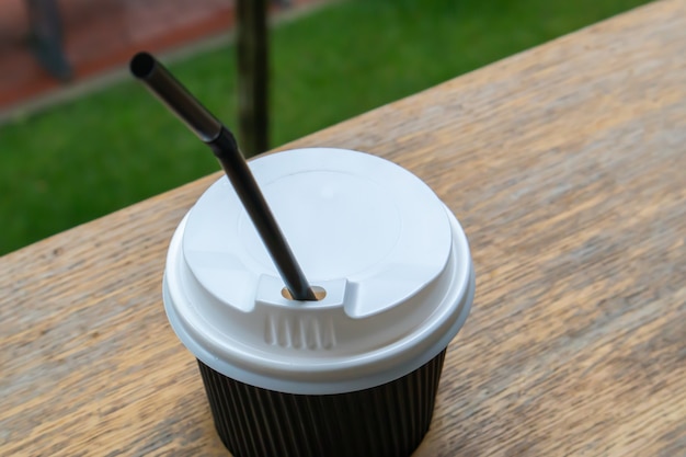 Eine schwarze Papierkaffeetasse mit Deckel im Sommer im Freien bei sonnigem Wetter auf einem Holztisch eines Cafés, Cafés oder Restaurants.