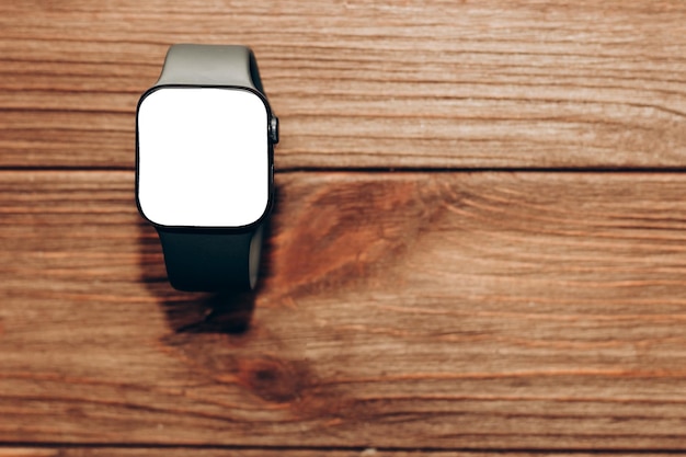 Eine schwarze technologische Smartwatch liegt auf einem Holzhintergrund mit einem weißen Bildschirm für Textraum