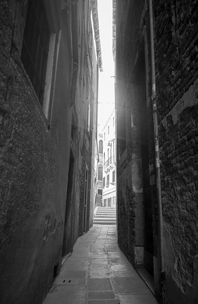 Eine sehr enge leere Gasse mit Backsteinmauern und einem starken Licht vor dem Himmel