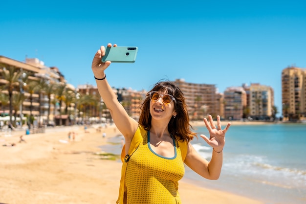 Eine sehr glückliche junge Frau, die ein Selfie mit dem Telefon in Playa del Cura in der Küstenstadt Torrevieja, Alicante, valencianische Gemeinschaft nimmt