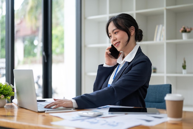 Eine selbstbewusste asiatische Geschäftsfrau spricht am Telefon mit ihrem Kunden, während sie an ihrem Schreibtisch arbeitet