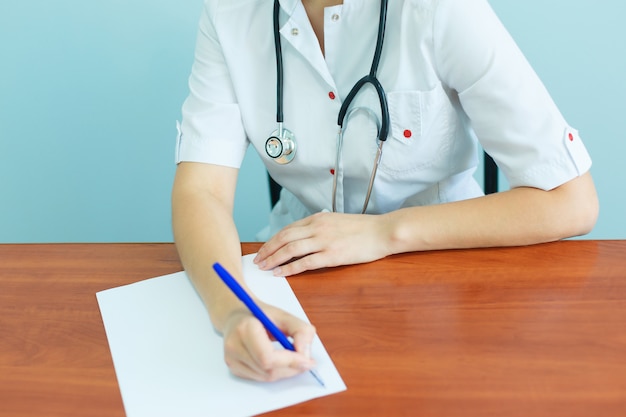 Eine selbstbewusste Ärztin mit einem Stethoskop sitzt am Tisch und schreibt Empfehlungen an die Patientin.