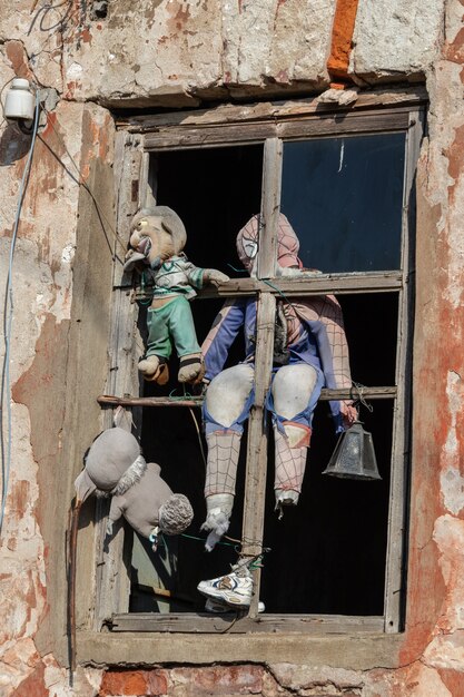 Eine seltsame alte zerrissene Puppe in einem Holzfenster in der orangefarbenen Wand eines alten verlassenen Hauses