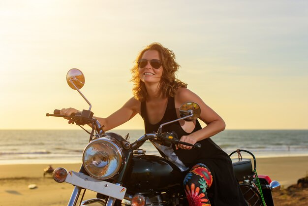 Eine sexy junge Frau mit Sonnenbrille sitzt auf einem schwarzen Chrommotorrad