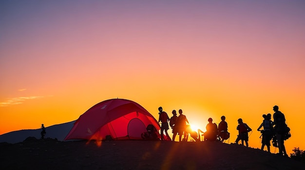 Eine Silhouette einer Gruppe von Menschen vergnügt sich während des Sonnenuntergangs auf dem Gipfel des Berges in der Nähe des Zeltes