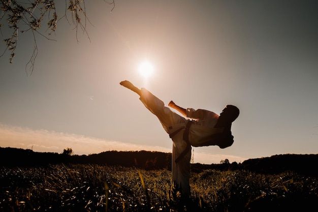 Eine Silhouette eines Karate-Kämpfers im weißen Kimono-High-Kick auf dem Hintergrund des Sonnenuntergangs