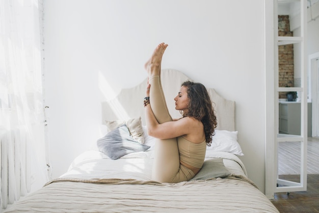 Eine sportliche Frau, die Yoga macht, die Paripurna Navasana-Übung durchführt, Balance-Pose, zu Hause oder in einem Yoga-Studio mit weißen Wänden.