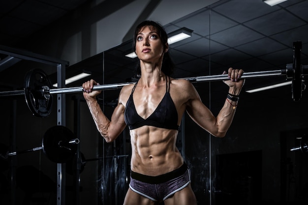 Eine sportliche Frau in einem schwarzen Top und Shorts, die mit einer Bar in der Sporthalle an den Händen trainieren Fittes Mädchen, das einen aktiven Lebensstil führt