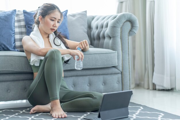 Eine sportliche Frau in Sportkleidung trainiert, während sie sich zu Hause auf ihrem Tablet Online-Trainingseinheiten ansieht