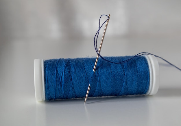 Eine Spule aus blauem Faden mit einer Nadel Nähwerkstatt-Atelier