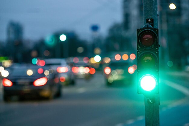 eine Stadtüberquerung mit einem Semaphore auf verschwommenem Hintergrund mit Autos in den Abendstraßen grünes Licht