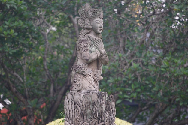 Eine Statue einer Frau mit Kopf und Armen vor einem Baumstamm.