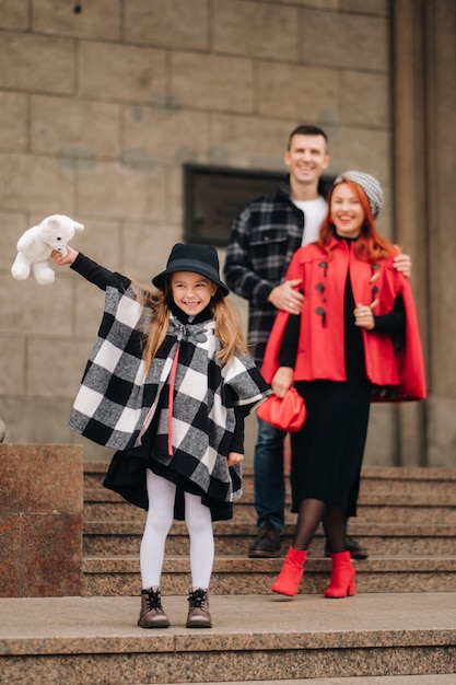 Eine stilvolle dreiköpfige Familie ist im Herbst in der Stadt und das Mädchen mit dem Stofftier ist fröhlich