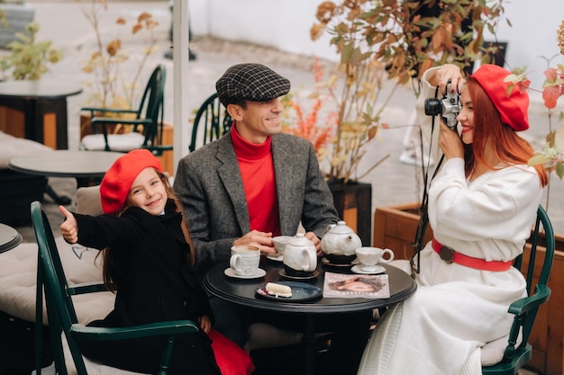 Eine stilvolle dreiköpfige Familie sitzt an einem Tisch draußen in einem Café und trinkt Kaffee Vater, Mutter und Tochter in der Herbststadt