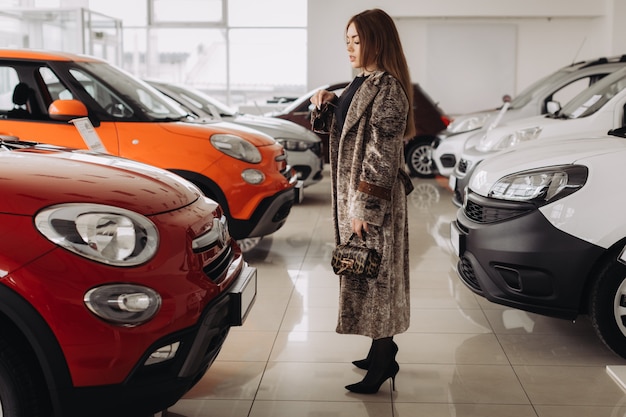 Eine stilvolle junge Frau wählt ein neues Auto in einem Autohaus