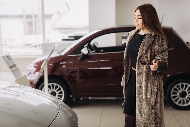 Eine stilvolle junge Frau wählt ein neues Auto in einem Autohaus