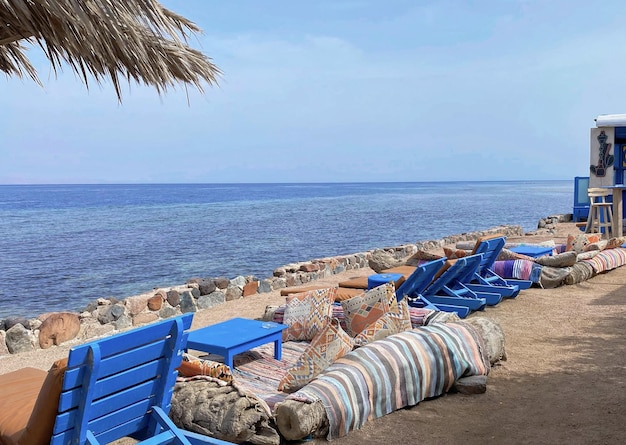 Eine Strandszene mit blauen Stühlen und einem Strohschirm am Strand.