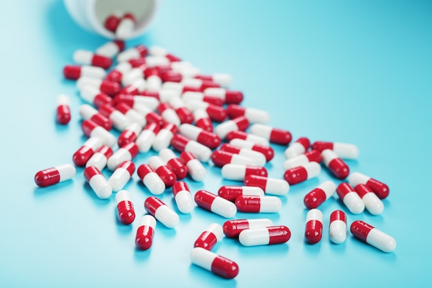 Eine Streuung von roten und weißen Tablettenkapseln aus einem weißen Glas auf blauem Grund. Arzneimittel, Medizin, Vitamine