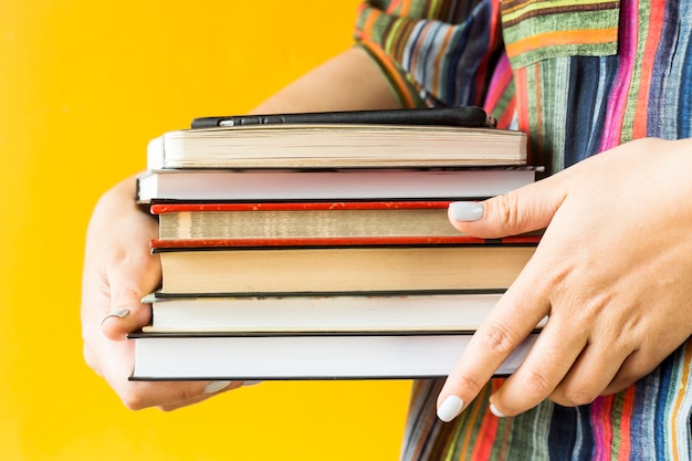Eine Studentin in einem gestreiften Hemd hält einen Stapel Lehrbücher in ihren Händen