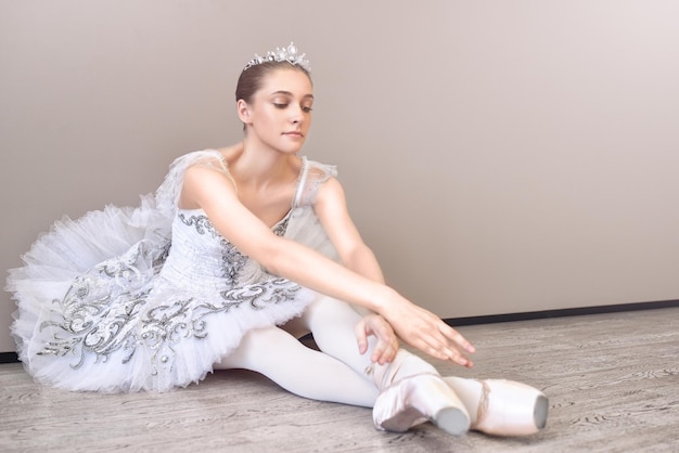 Eine süße Ballerina, die mit nach vorne ausgestreckten Armen auf dem Boden sitzt und Ballettposen im Studio übt