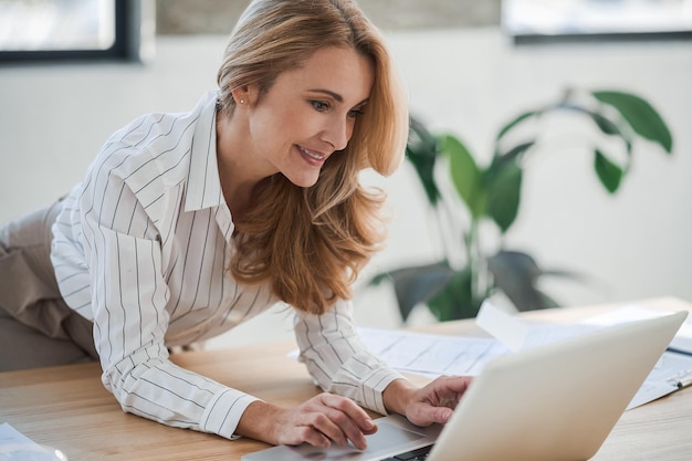 Eine süße, elegante Frau im Büro, die am Laptop arbeitet