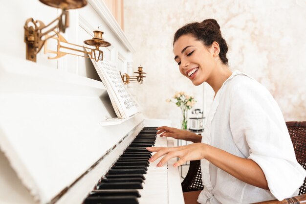 Foto eine süße fröhliche positive dame im weißen hemd spielt zuhause klavier.