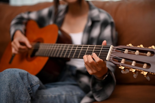 Eine talentierte Frau entspannt sich in ihrem Wohnzimmer und spielt ihr beschnittenes Bild der Akustikgitarre