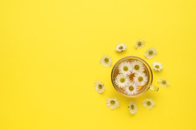 Eine Tasse Blumentee und verstreute Blumen auf gelbem Grund. Medizinischer Tee.