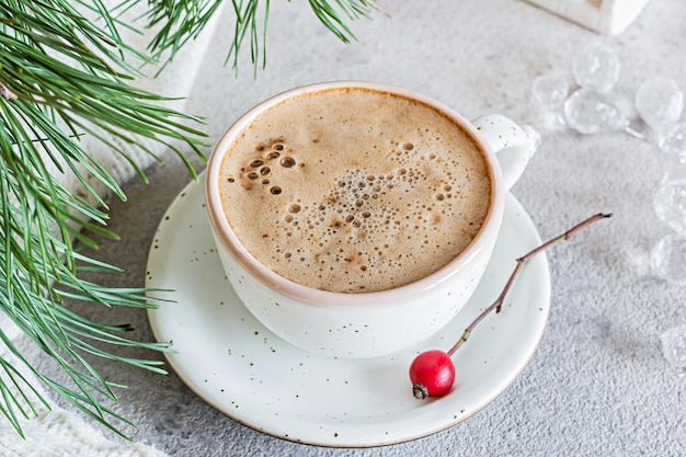 Eine Tasse Cappuccino (lat) auf hellem Hintergrund neben einem Weihnachtsbaum und Dekorationen.