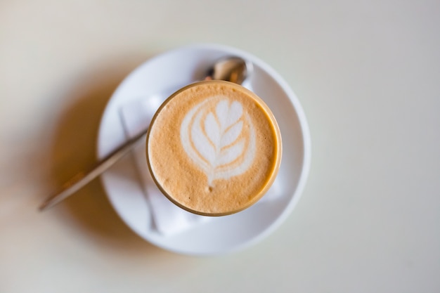 Eine Tasse Cappuccino mit Latte Art auf weißem Holztisch, weiße Keramikschale, Draufsicht. Cafe Kultur.