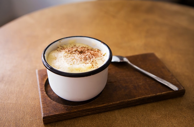 Eine Tasse Cappuccino steht auf einem Holztisch und steht für einen Löffel