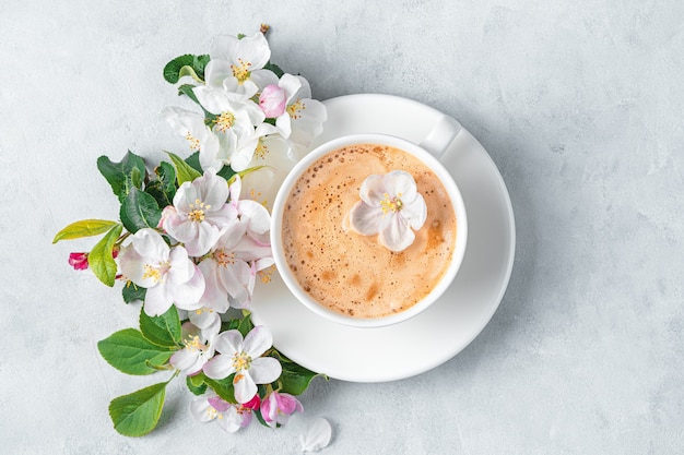 Eine Tasse Cappuccino und Blumen an einer grauen Wand