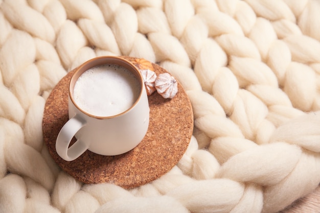 Eine Tasse Cappuccino und Kekse auf dem Hintergrund einer Decke aus dickem Garn. Die Atmosphäre von Wohnlichkeit und Behaglichkeit