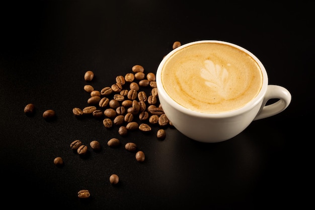 Eine Tasse Cappuccinoin weiße Tasse und Kaffeebohnen auf schwarzem Hintergrund, Draufsicht