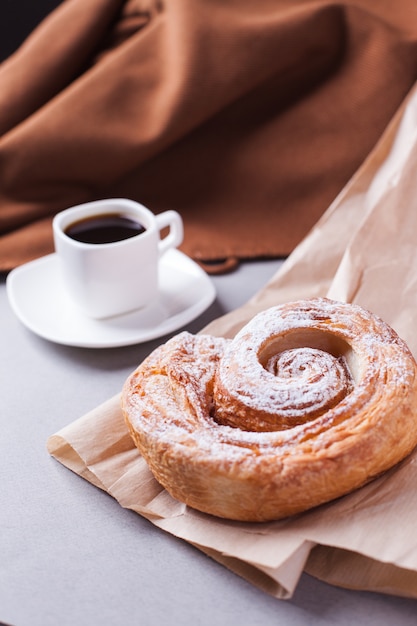 Eine Tasse Espresso auf einer Untertasse und ein Blätterteig in King Size