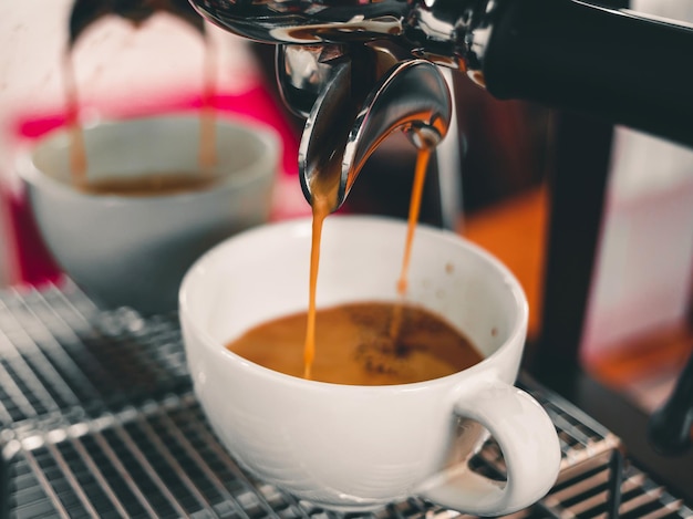 Eine Tasse Espresso, die aus der Kaffeemaschine fließt und in die Kaffeetasse fließt, macht Kaffee im Café