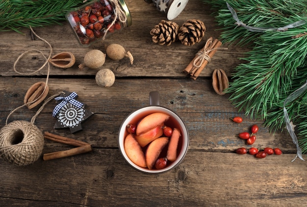 Eine Tasse Glühwein mit Früchten, Beeren und Zimt auf einem hölzernen Hintergrund.