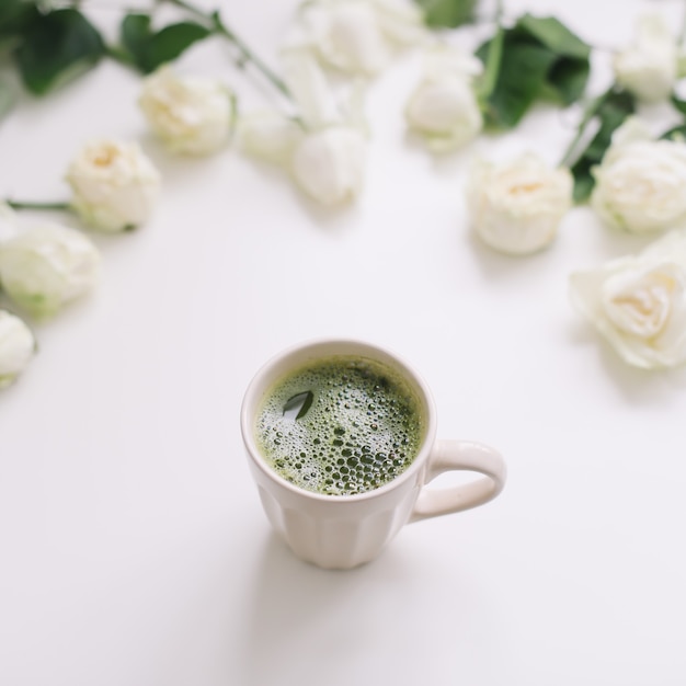Eine Tasse grüner Matcha-Tee mit weißen Rosen auf weißer Ansicht von oben