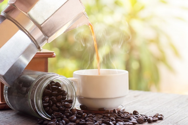 Eine Tasse heiße Espresso-Kaffeetassen und geröstete Kaffeebohnen mit Moka-Kanne auf Holzbodenhintergrund, Kaffeemorgen, selektiver Fokus