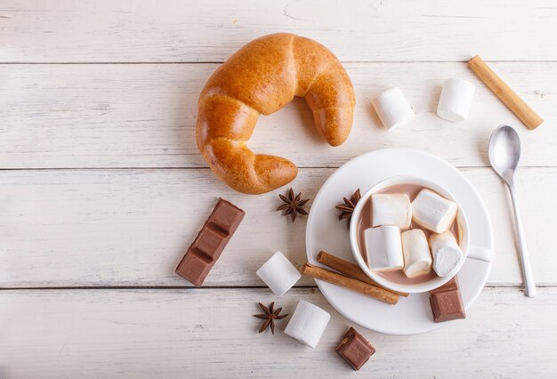 Eine Tasse heiße Schokolade mit Marshmallow, Croissant und Gewürzen