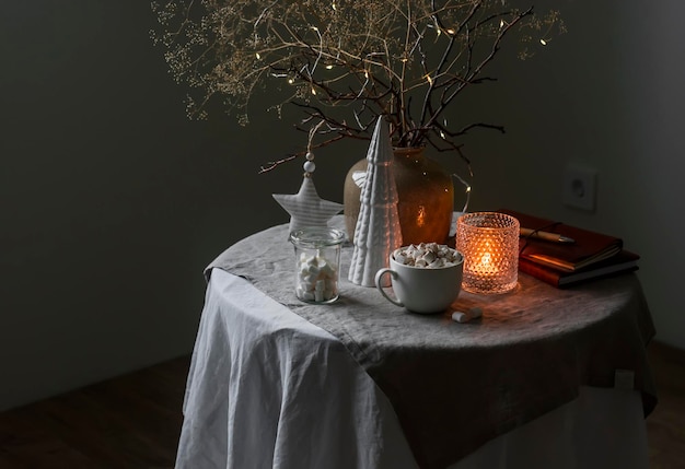 Eine Tasse heiße Schokolade mit Marshmallows Weihnachtsdekor beleuchtete Kerze auf dem Tisch in einem gemütlichen Wohnzimmer im skandinavischen Stil