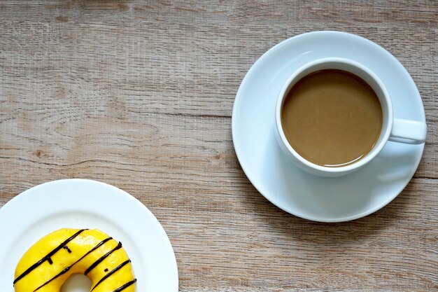 Eine Tasse heißen Kaffee mit gelben süßen Donuts auf Holzuntergrund