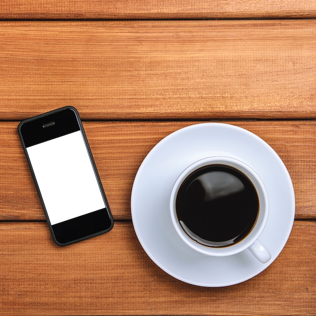 Eine Tasse heißen Kaffee und Handy auf einem hölzernen Hintergrund.