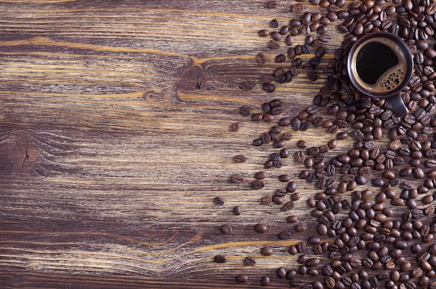 Eine Tasse heißen Kaffees und verstreute Bohnen befindet sich auf einer alten Holzoberfläche, Draufsicht mit Platz für Text